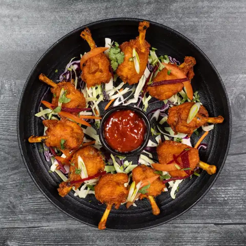 Taj Mahal Indian Restaurant's chicken lollipops, garnished with shredded cabbage, carrots, and cilantro, with a red dipping sauce.