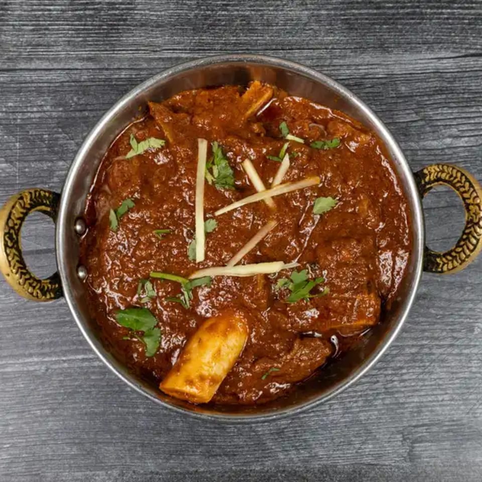 Taj Mahal Indian Restaurant's lamb rogan josh, a rich red curry with tender lamb, garnished with ginger and cilantro.