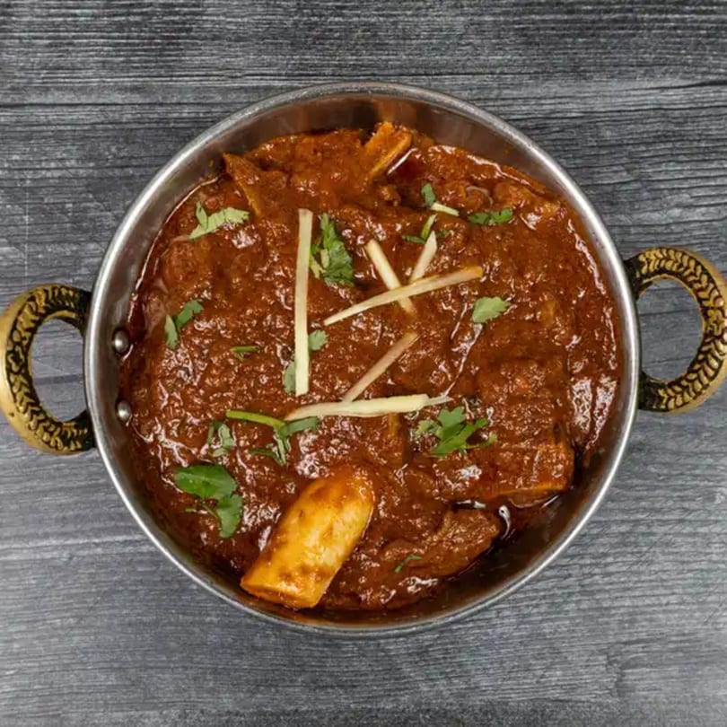 Taj Mahal Indian Restaurant's lamb rogan josh, a rich red curry with tender lamb, garnished with ginger and cilantro.