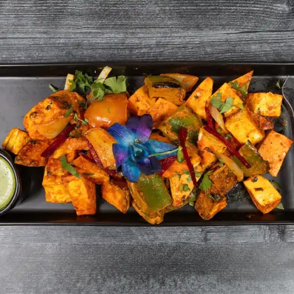 Paneer tikka with bell peppers, onions, and cilantro, garnished with an orchid, served with green chutney.