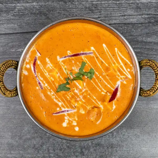 Taj Mahal Indian Restaurant's butter chicken, garnished with cilantro and cream swirls in a metal bowl.