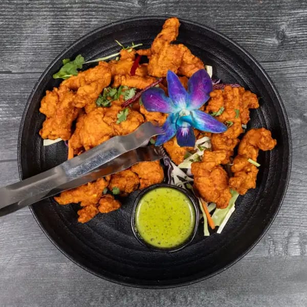 Taj Mahal Indian Restaurant's chicken pakora, garnished with a purple orchid and served with green chutney.