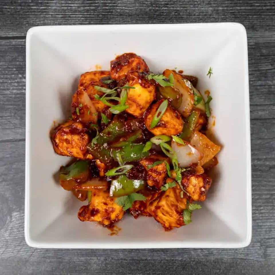 Chili Paneer, a spicy Indian dish with paneer, bell peppers, and onions in a white bowl.