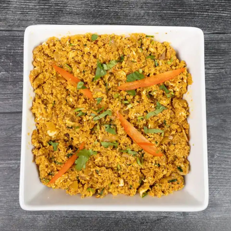 Scrambled paneer dish, garnished with fresh cilantro and red pepper slices, in a white square bowl.